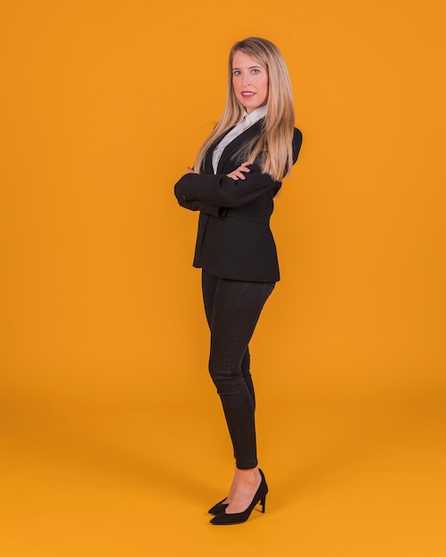 Confident young woman standing against an orange backdrop