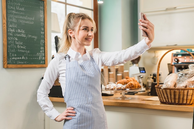 彼女のコーヒーショップで携帯電話からselfieを取って自信を持って若い女性