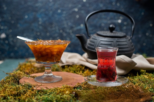 Confiture, tea glass and kettle on the grass board