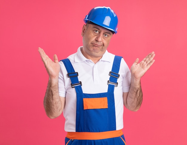 L'uomo caucasico adulto confuso del costruttore in uniforme sta con le mani alzate isolate