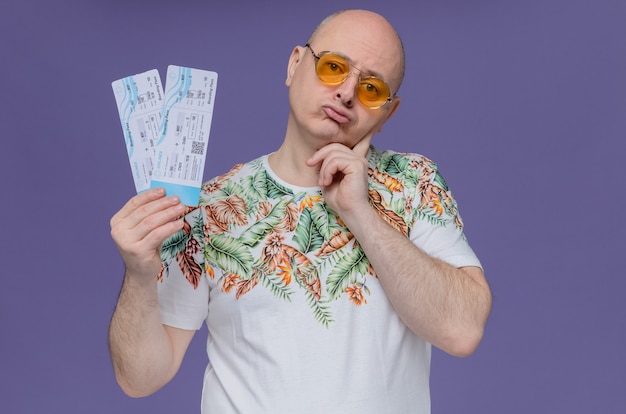 Confused adult man with sunglasses holding air tickets 