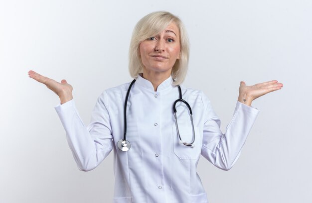 Confused adult slavic female doctor in medical robe with stethoscope keeping hands open isolated on white background with copy space