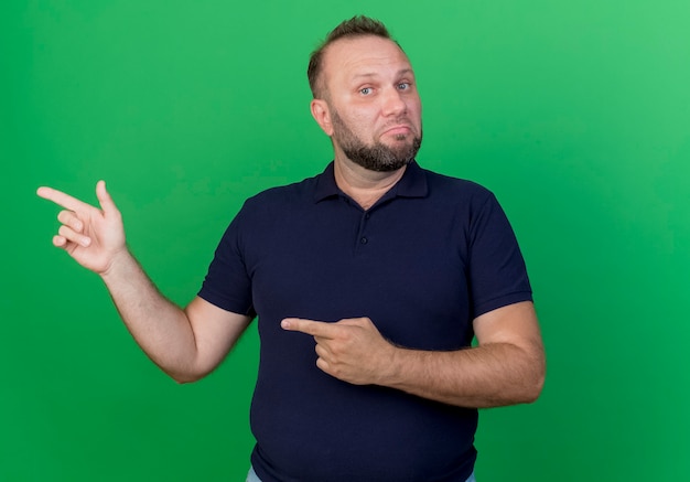 Confused adult slavic man looking and pointing at side isolated