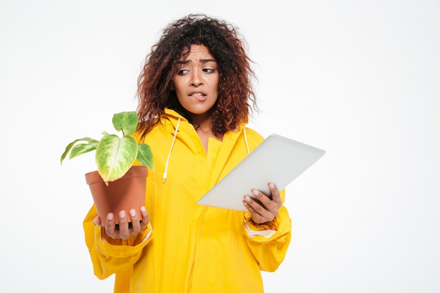 Confused african woman in raincoat holding plant