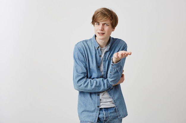 Confused angry fair-haired young male student gestures in bewilderment, expresses negative emotions as has conversation with girlfriend who critises him. Good-looking caucasian guy in confusion