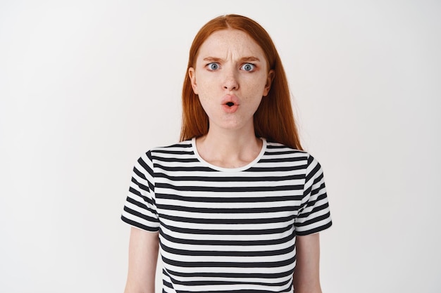 Free photo confused and angry redhead girl frowning, asking wtf and staring at front puzzled, standing over white wall