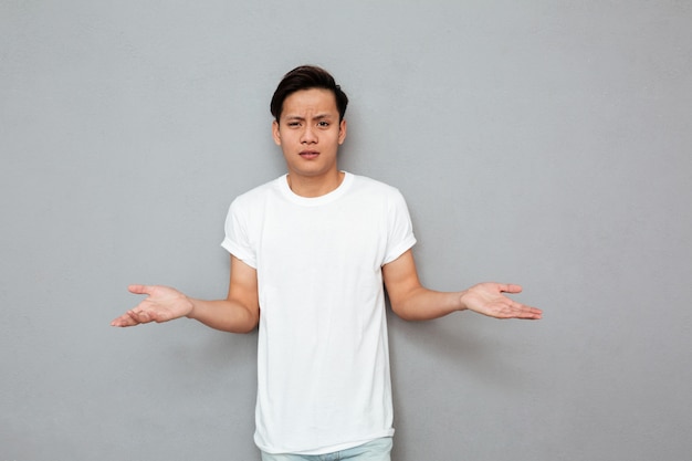 Confused asian man standing over grey wall