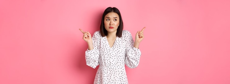 無料Photo 混乱したアジアの女性は躊躇し、肩をすくめ、両手を指差して優柔不断に見つめ、hが必要です
