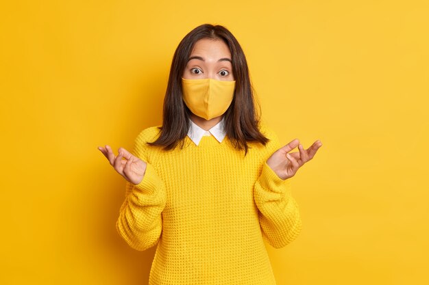 confused Asian woman wears protective mask spreads palms and looks hesitant doesnt know how to stop virus epidemic disease.