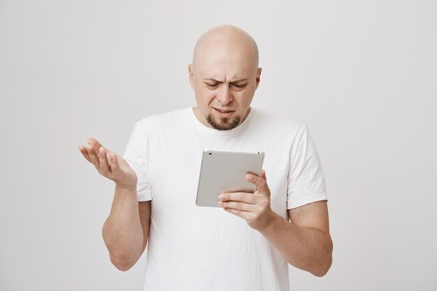 Confused bald adult man staring puzzled at digital tablet