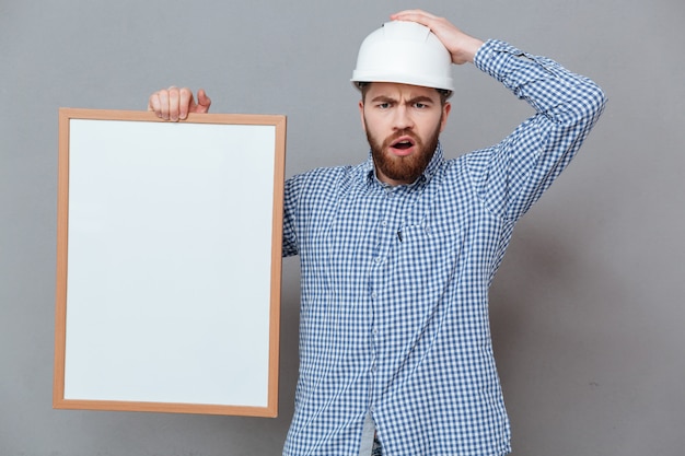 Confused bearded builder holding blank board