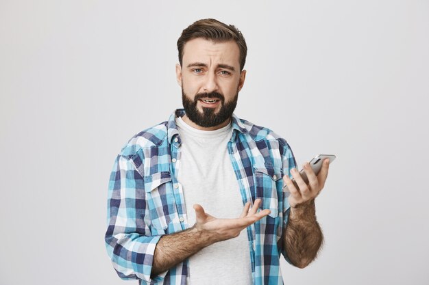 あごひげを生やした男が肩をすくめて、携帯電話アプリの使い方がわからない