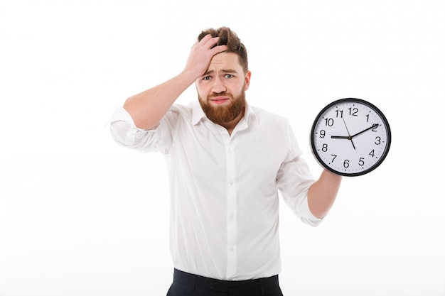 Confused bearded man in business clothes holding clock