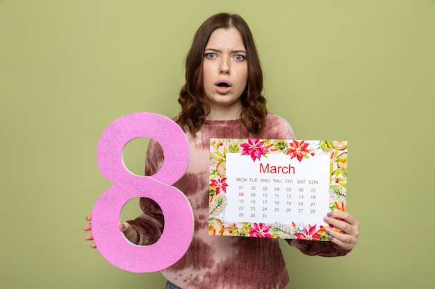 Free photo confused beautiful young girl on happy women's day holding number eight with calendar