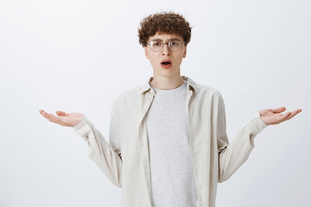 Free photo confused and bothered teenage guy posing against the white wall