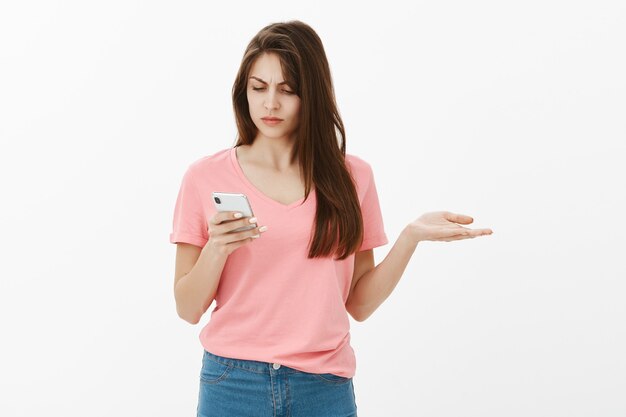彼女の電話でスタジオでポーズをとって混乱しているブルネットの女性