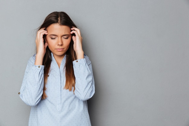 Confused brunette woman in shirt with closed eyes having headache