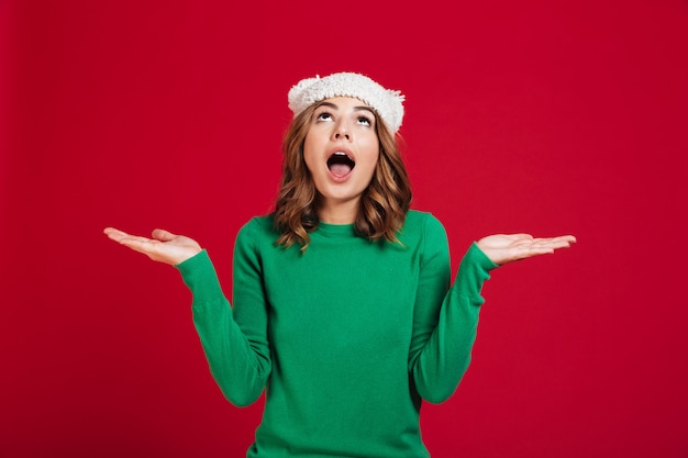 Free photo confused brunette woman in sweater and funny hat shrugs shoulders