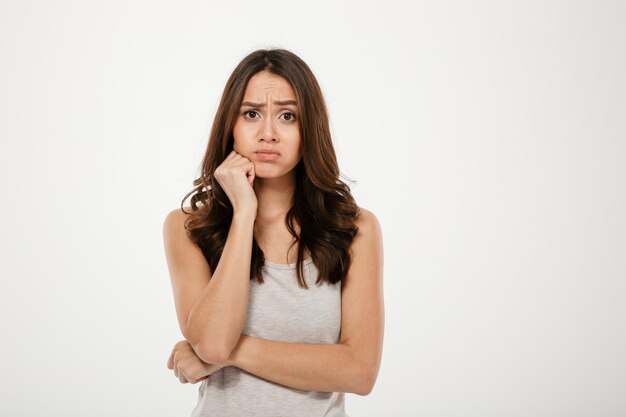 Confused brunette woman with arm near chin looking at the camera over gray