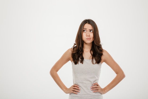 Confused brunette woman with arms on hips looking away over gray
