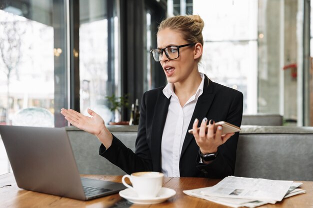 Confused business woman using laptop computer and phone