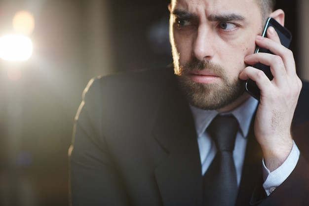 Confused businessman speaking by smartphone