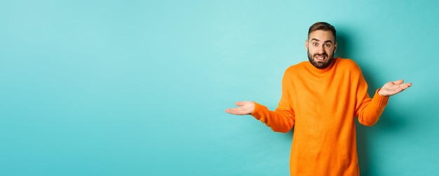 Foto gratuita uomo caucasico confuso con la barba che si stringe nelle spalle e sembra incapace di stare in piedi indeciso contro il turchese