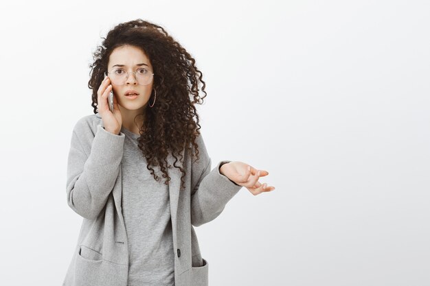 confused clueless caucasian businesswoman in trendy eyewear and coat, raising palm questioned and staring frustrated