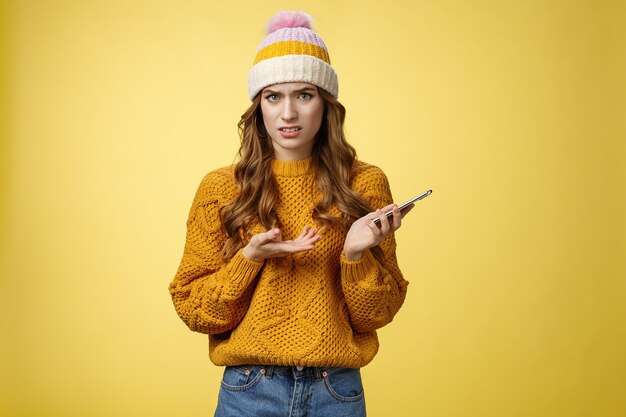 Confused cringing annoyed young woman shocked how friend talked her frowning raise hand dismay look frustrated camera holding smartphone finish video call unpleasant note, yellow background