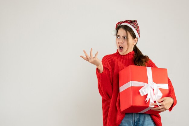 confused cute girl with santa hat holding present standing on white