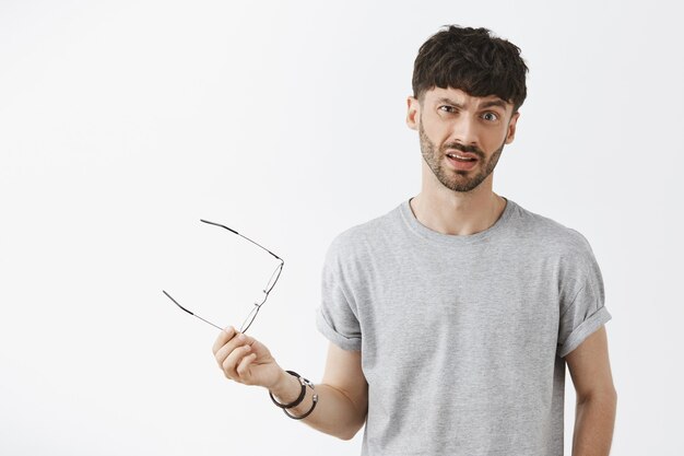 Confused and disappointed handsome guy posing against the white wall