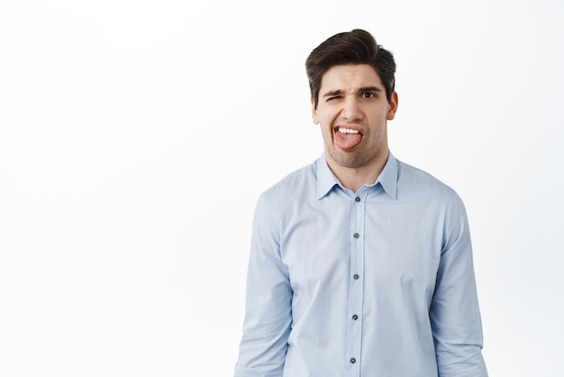 Confused and disgusted young man office guy showing tongue and complain on bad tasty something awful dislike white background