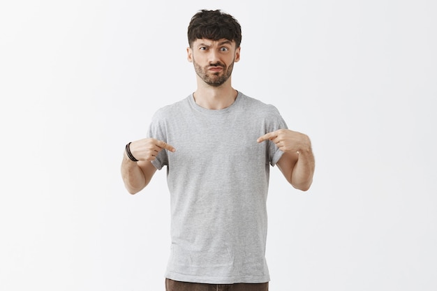 Confused and doubtful handsome guy posing against the white wall