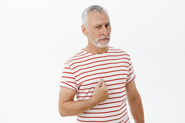 Confused elderly man pointing at himself puzzled