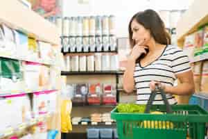 Бесплатное фото Смущенная покупательница выбирает продукты питания на полке в супермаркете
