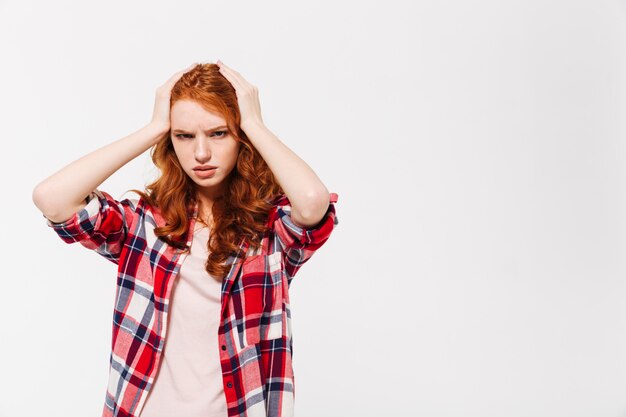 Confused ginger woman in shirt holding head and looking away