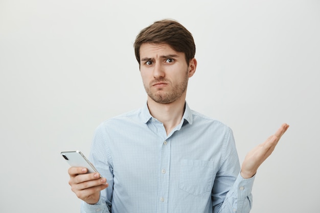 Confused handsome guy shrugging, can't understand message in phone