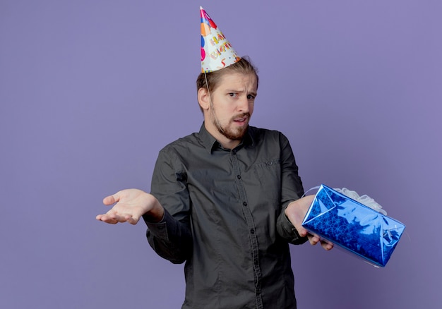 생일 모자에 혼란 된 잘 생긴 남자는 보라색 벽에 고립 된 선물 상자를 보유