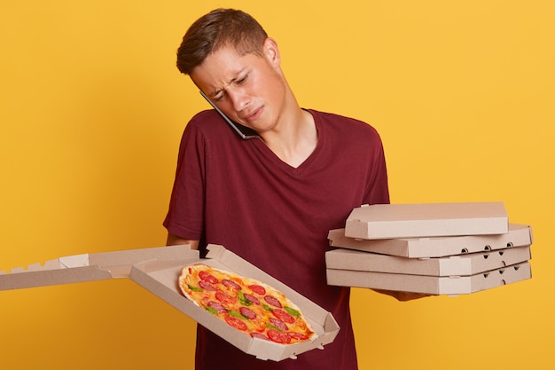 Foto gratuita uomo di consegna confuso duro lavoro parlando al telefono con il cliente, non conoscendo l'indirizzo, avendo problemi, tenendo scatole di cartone con pizza