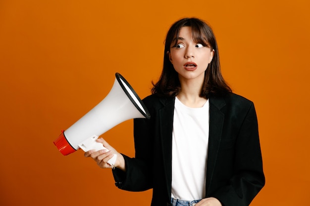 Free photo confused holding loudspeaker young beautiful female wearing black jacket isolated on orange background