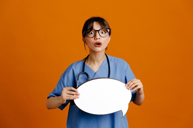 Confused holding speech bubble young female doctor wearing uniform fith stethoscope isolated on orange background