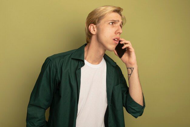 緑のTシャツを着ている若い金髪の男が電話で話す側を見て混乱