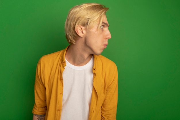 Free photo confused looking at side young blonde guy wearing yellow t-shirt isolated on green with copy space