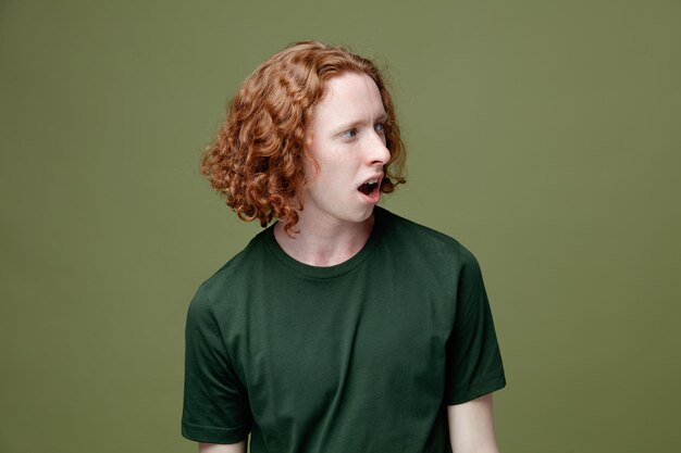 Confused looking at side young handsome guy wearing green t shirt isolated on green background