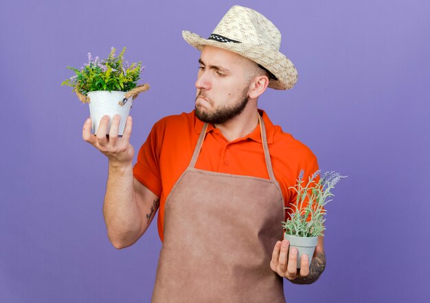 園芸帽子をかぶって混乱している男性の庭師は植木鉢を保持します