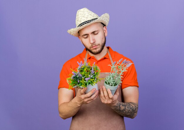 Confused male gardener wearing gardening hat holds and looks at flowerpots 