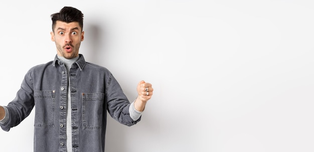 Free photo confused man holding big size object and looking shocked shaping large thing standing on white backg