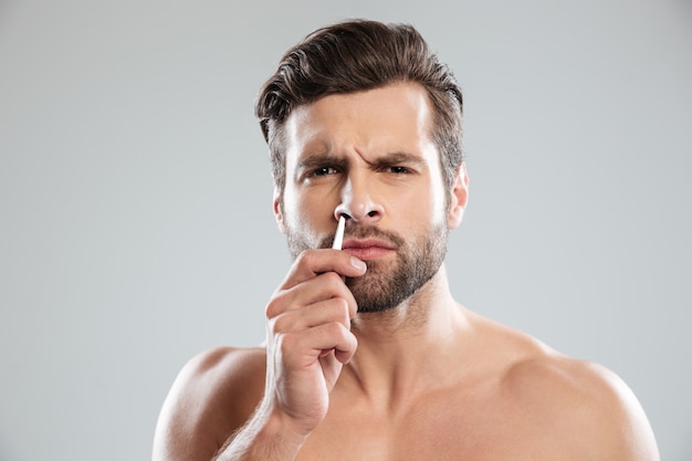 Confused man trying to tweezer hair in nose