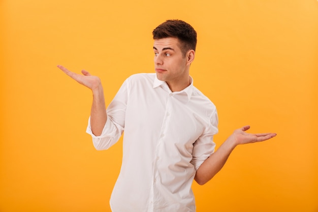 Confused man in white shirt shrugs his shoulder and looking away