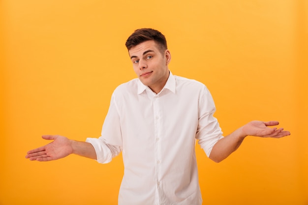 Confused man in white shirt shrugs his shoulder and looking at the camera